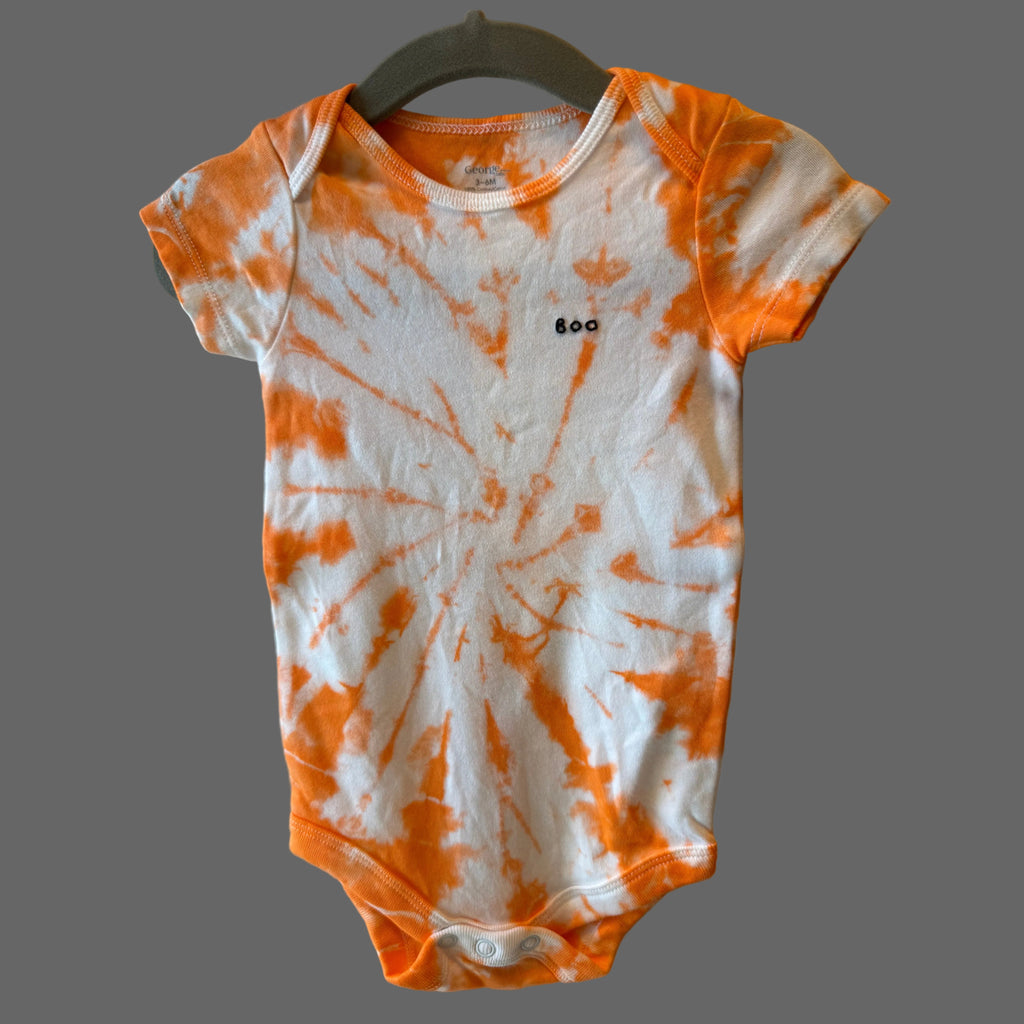 An infant short-sleeve bodysuit with an orange and white tie-dye spiral featuring a small black hand embroidered BOO on the chest.