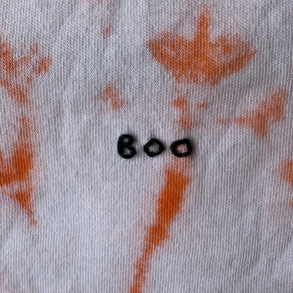 Close-up of an orange tie-dye onesie with hand embroidered BOO. 