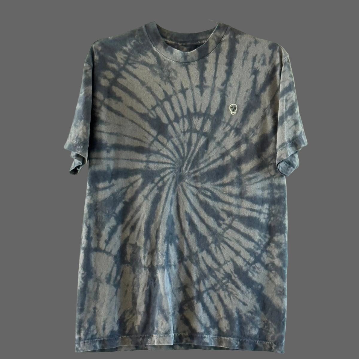 A short-sleeve cotton crewneck t-shirt featuring a black on faded black spiral tie-dye pattern with a hand embroidered skull on the upper right chest area.