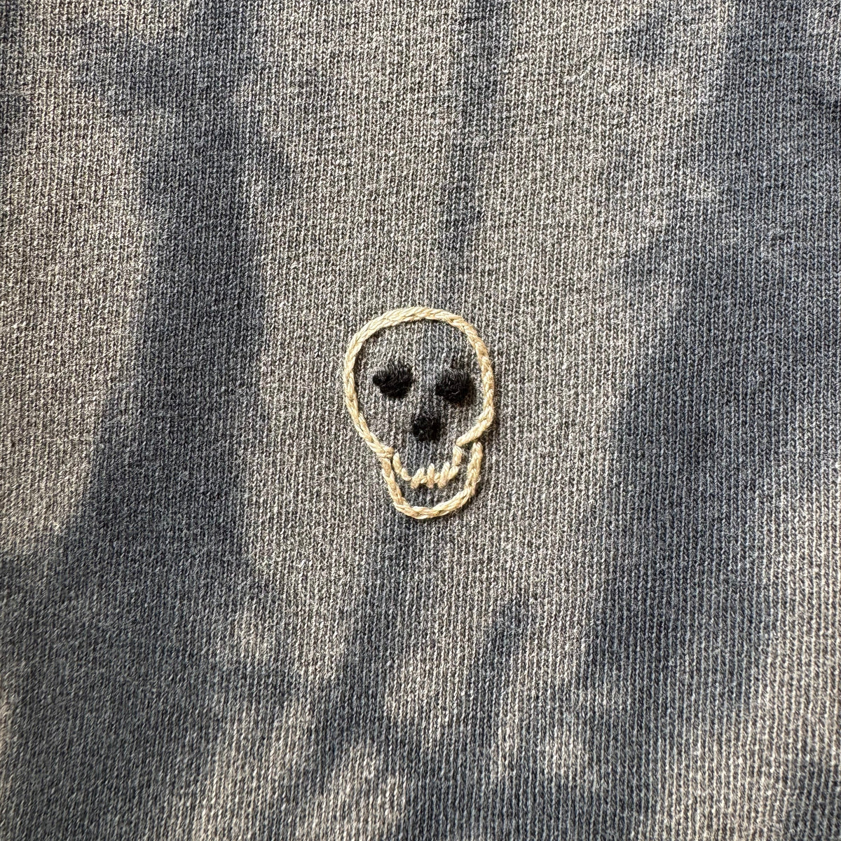 Close-up of a black on faded black tie dyed cotton shirt with a small hand embroidered skull detail.