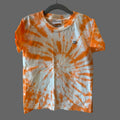 A short-sleeve cotton crewneck t-shirt with an orange and white tie-dye spiral pattern with a small black hand embroidered jack-o-lantern face on the left chest area.